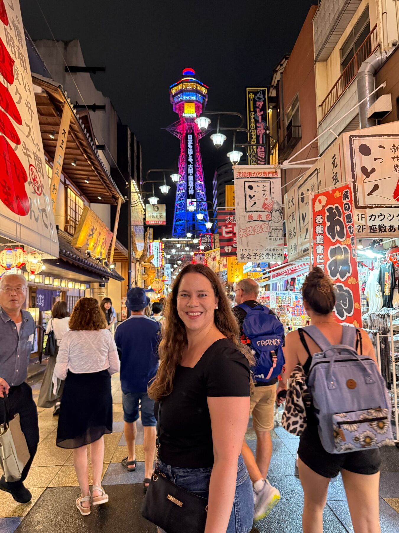 A traveler smiling beneath the illuminated Tsūtenkaku tower in Osaka
