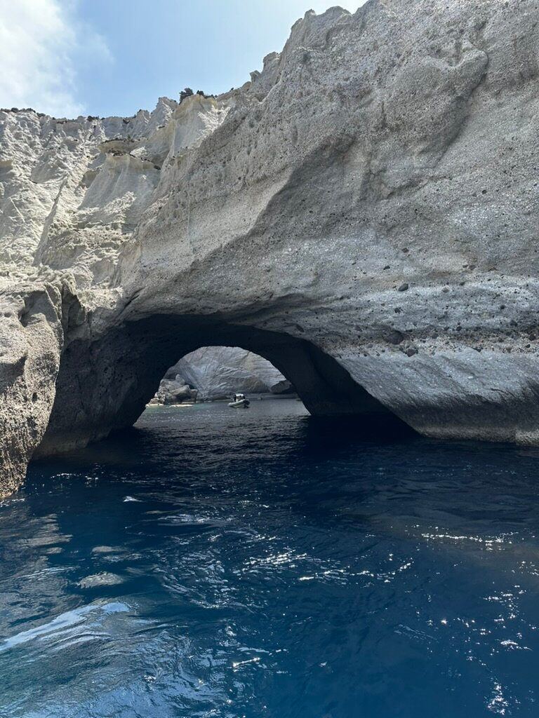 A sea cave opening through pale volcanic cliffs above deep blue water in Milos