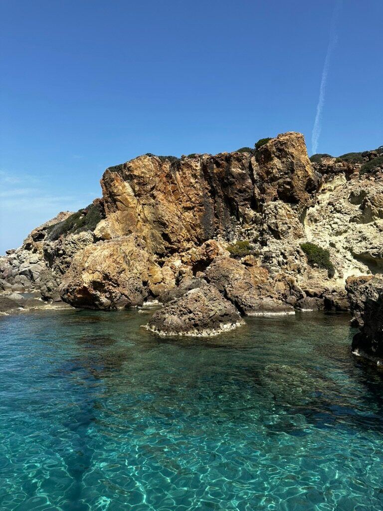 Clear turquoise water meeting rugged volcanic rocks along the coast of Milos