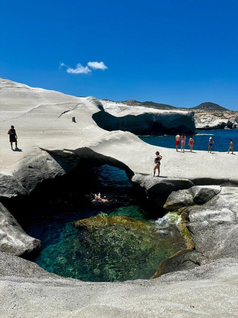 White volcanic rock formations and a clear swimming cove at Sarakiniko Beach in Milos