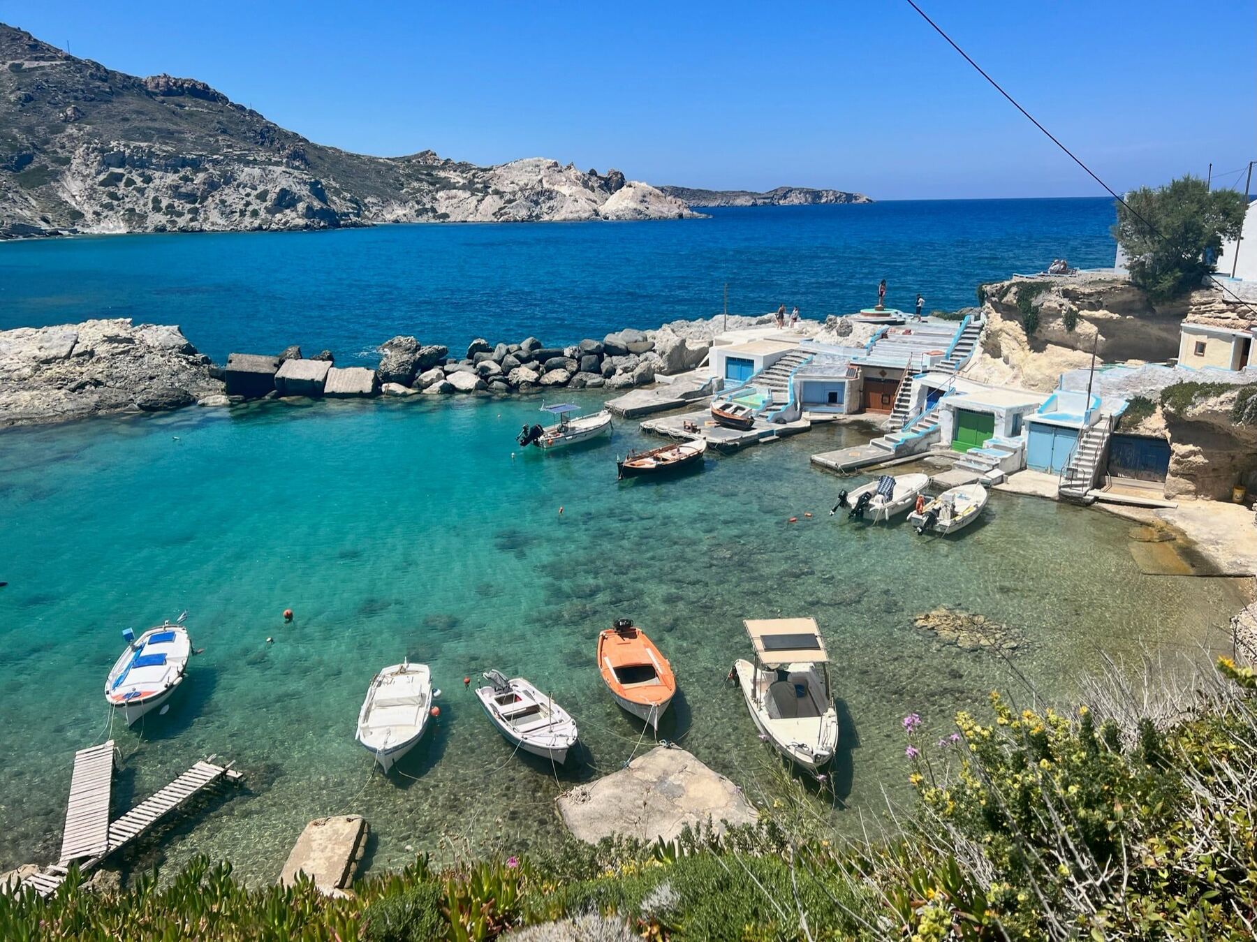 Colorful fishing boats and white boathouses beside clear turquoise water in Milos