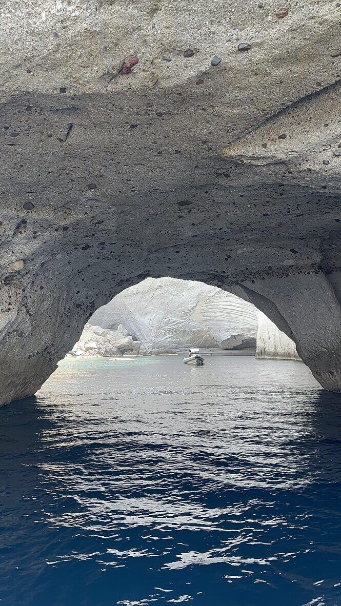 A small boat framed by a sea cave in Milos, Greece