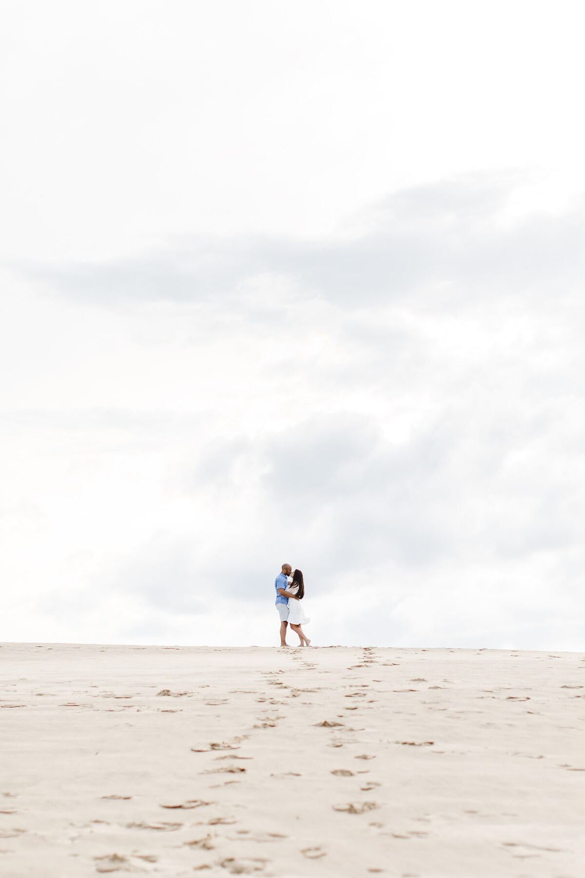 A couple embracing on pale sand beneath an expansive sky